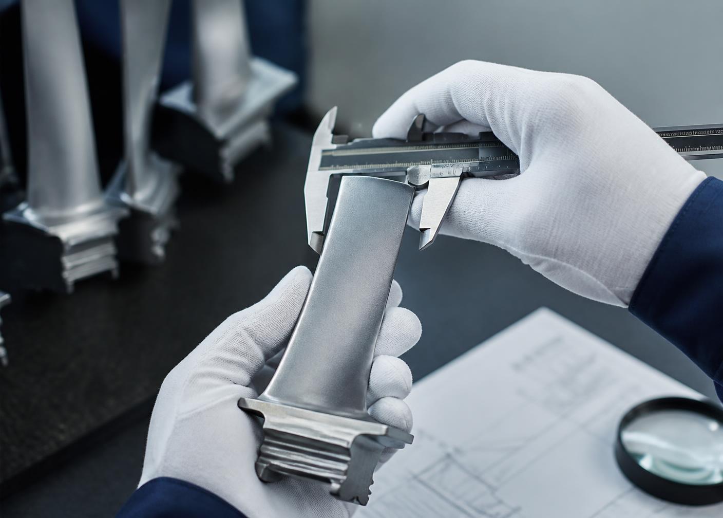 Technician measuring an aircraft turbine blade with calipers during inspection
